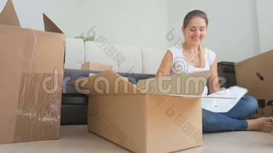 年轻女子坐在地板上，用纸板<strong>箱</strong>包装花瓶和杯子