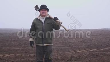 戴着帽子的高级农民，手里拿着一把泥泞的<strong>锄头</strong>和田野上的草叉。 体力劳动。 福克