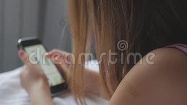 年轻女孩坐在床上，用电话做网上购物。 网上购物的概念。