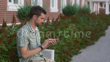休闲打扮的男人坐在长凳上，用他的智能<strong>手表</strong>和智能<strong>手机</strong>