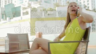年轻优雅的女人在游泳池附近的露台上等男朋友。 背景城市景观