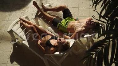 在游泳池附近晒日光浴。 美丽的男人和女人躺在日光浴床上。 日落，日出