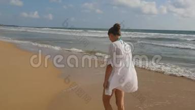 美丽的女人穿着泳衣和衬衫在海边散步，举起双手。 年轻女孩在海边