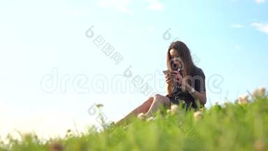穿黑色皮衣的漂亮黑发女孩在<strong>草坪</strong>上用智能手机。 4K<strong>视频</strong>