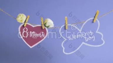 妇女节`快乐.. 妇女节`纸上，挂在一根绳子上，靠近粉红色的纸心，蓝色的背景上有花。