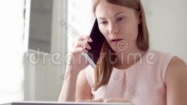忙碌的女人坐在家里拿着笔记本电脑和智能手机。 通过手机在屏幕上讨论项目