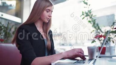穿着黑色夹克的金发女孩坐在咖啡馆A©里。 她<strong>喝了</strong>一杯咖啡，用笔记本工作。