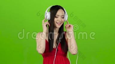 女孩通过耳机听欢快而充满活力的音乐。 绿色屏幕。 慢动作
