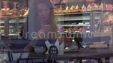 漂亮的黑发女孩在咖啡馆里用她的智能手机。 从外面透过窗户观看。 4K视频
