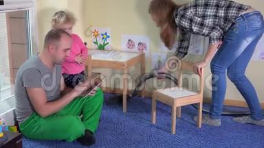 懒惰的父亲和小女儿使用平板电脑和母亲胡佛地板