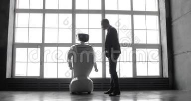 一个时尚的男人与机器人交流，把一只塑料<strong>机械</strong>手<strong>臂</strong>按在机器人身上，握手。 控制系统