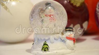 圣诞装饰品。 雪落在闪闪发亮的神奇水晶球里，背景是雪人和圣诞球。 白雪覆盖的穹顶