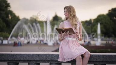 夏天公园喷泉里一个年轻迷人的女孩饶有兴致地读着一本书