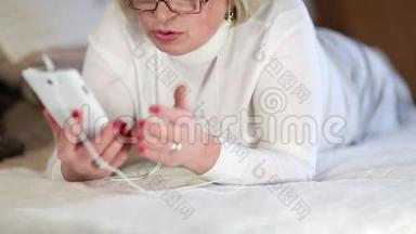 带着白色智能手机的老妇人躺在床上