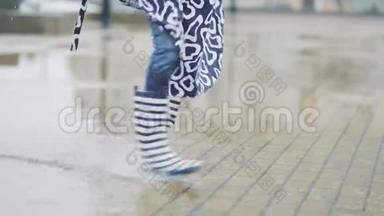 大雨过后，穿着橡胶靴的女孩在水坑里奔跑和跳跃。 女人在雨后玩得很开心。 慢动作