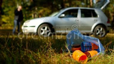 一包带塑料瓶的垃圾躺在大自然上，背景中有一辆车，人们都是
