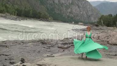 年轻的女人穿着一件长长的流动的衣服在河山的背景上。 给一个在绿色中盘旋的女人上色