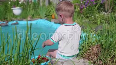 那个男孩坐在一个小湖边。 这孩子用脚造成水溅. 夏日炎炎。 快乐的童年