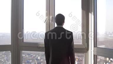 年轻的成功商人站在窗户前，眺望城市的远方。 慢动作。 3840x2160