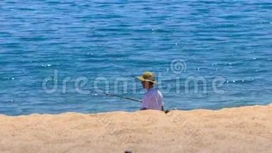 渔人戴着帽子，用鱼竿在沙滩上拍打蔚蓝的大海