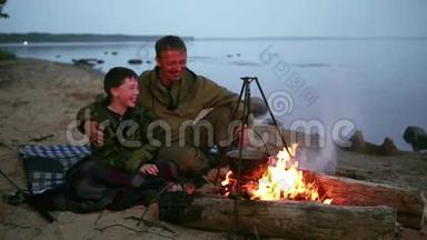 父子俩围坐在湖边的篝火旁..