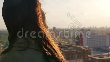 后景。 风吹长黑发美丽的年轻女人。 日落时站在屋顶上的女孩。 慢节奏