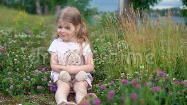 一个<strong>小女孩</strong>和一只玩具兔子在<strong>草地上</strong>的四叶草中玩耍