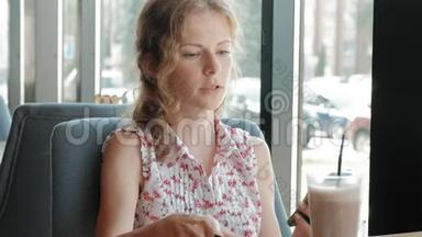 快乐的女孩喝咖啡，在咖啡馆里放松，微笑着看着智能手机