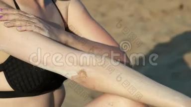穿着黑色泳衣的海滩上的女孩涂了<strong>防晒霜</strong>或<strong>防晒霜</strong>。 在海边的沙滩上