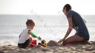 年轻的妈妈和小面包手在沙滩上玩沙子