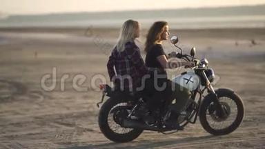 美丽的年轻女子摩托车手和他的女朋友骑摩托车在沙漠日落或日出。 骑自行车的女朋友