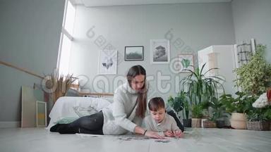 妈妈带着一个孩子在他家白色的内部和他的小儿子一起收集拼图。 快乐