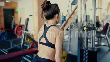 年轻漂亮的黑发女孩在健身房里留着长发，在健身房4k视频上做运动。
