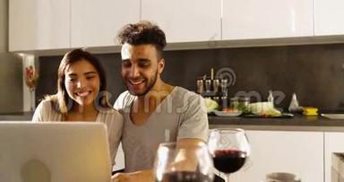 年轻混合种族夫妇使用笔记本电脑晨曦，快乐西班牙男人亚洲女人一起在厨房