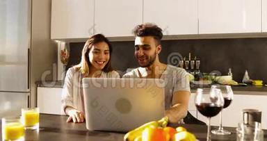 年轻混合种族夫妇使用笔记本电脑晨曦，快乐西班牙男人亚洲女人一起在厨房