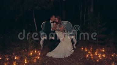 新婚夫妇在夜晚拥抱和亲吻，坐在黑暗的森林里的沙发上。