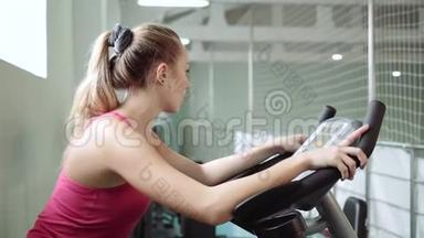 漂亮的女孩正在骑健身车锻炼。理念：热爱运动，参加健身房，适当的营养，苗条的身材