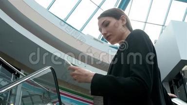 年轻的女商人肖像在自动扶梯上的电话交谈。 在商场或办公室工作的女商人