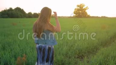夕阳下，一头直发的小女孩走在一片绿色的田野上。 平均射击。 慢动作