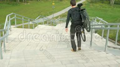 一个年轻人带着自行车穿过长长的楼梯。 在绿野的背景下.. 云云改变了光线