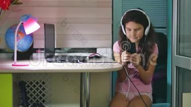 带着耳机坐着玩智能手机的少女。 在智能手机网络上玩网络游戏的女生
