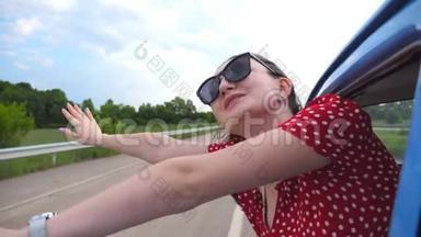 戴着太阳镜的快乐女孩斜靠在老式车窗外，享受旅行。 年轻女子望着窗外移动