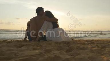 年轻的浪漫夫妇正在享受美丽的日落，坐在海滩上拥抱。 一个女人和一个男人坐在一起