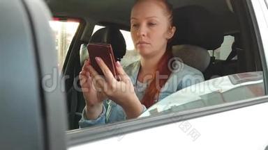 夏日夕阳西下，一位红发的年轻美女坐在汽车车轮后面，手里拿着手机