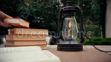 花园里桌子上有煤油灯和订书机。 手把书放在桌子上。 秋天
