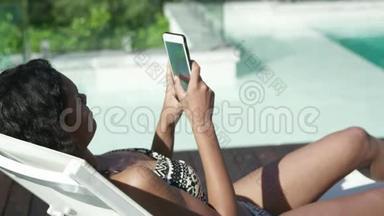 有魅力的女人躺在躺椅上用智能手机
