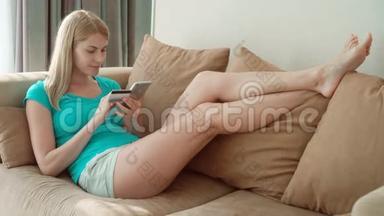 美丽迷人的年轻女子躺在沙发上，用智能手机刷卡上网