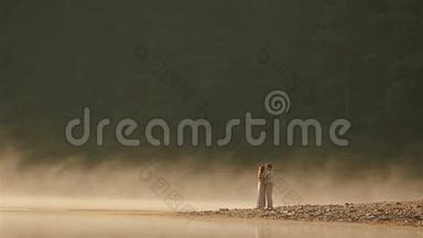 在风景如画的山湖上，一对身穿乌克兰民族服装的幸福乡村夫妇在夕阳下金色的薄雾中接吻