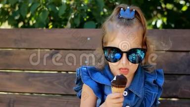 在阳光明媚的夏天，小女孩戴着太阳镜吃冰淇淋。 婴儿特写肖像