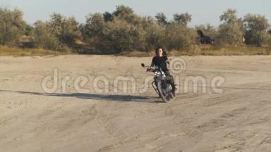 美丽的年轻女子骑着一辆古老的咖啡馆赛车<strong>摩托</strong>车在<strong>沙漠</strong>日落或日出。 女司机。 慢动作